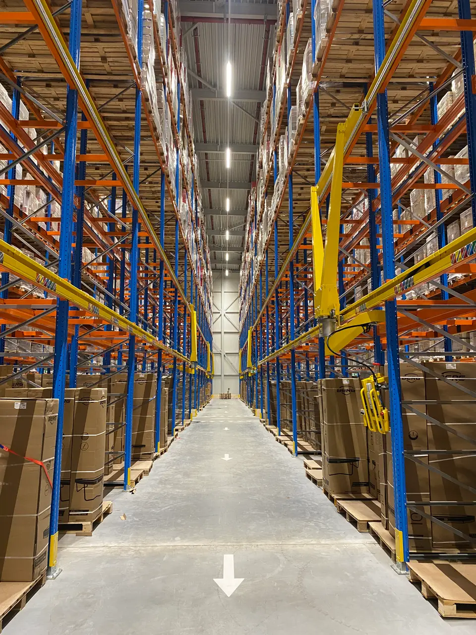 Magazijngang met twee RackJib-tilhulpen die aan de stelling zijn bevestigd